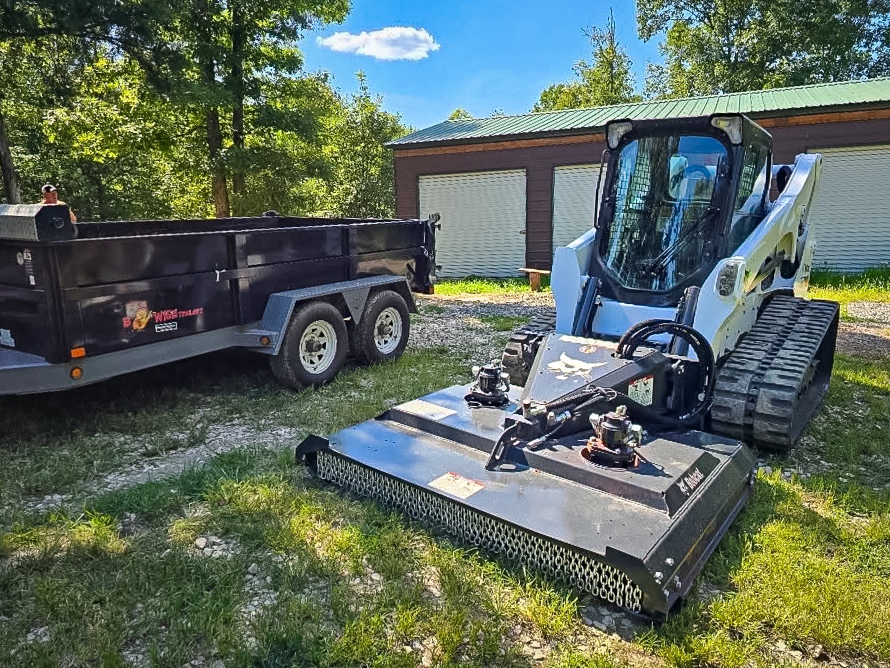 Bobcat T740 track loader with a brush cutter beside a dump trailer