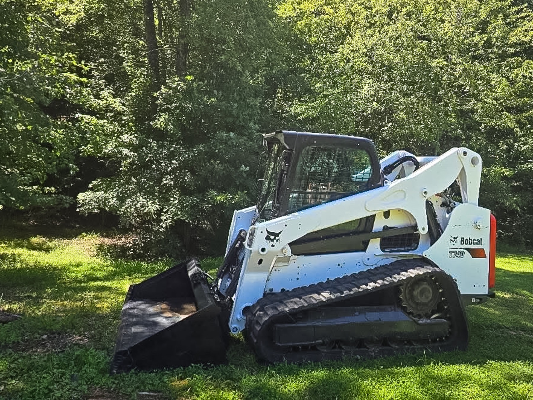 Bobcat T740 track loader with a bucket near a wooded area
