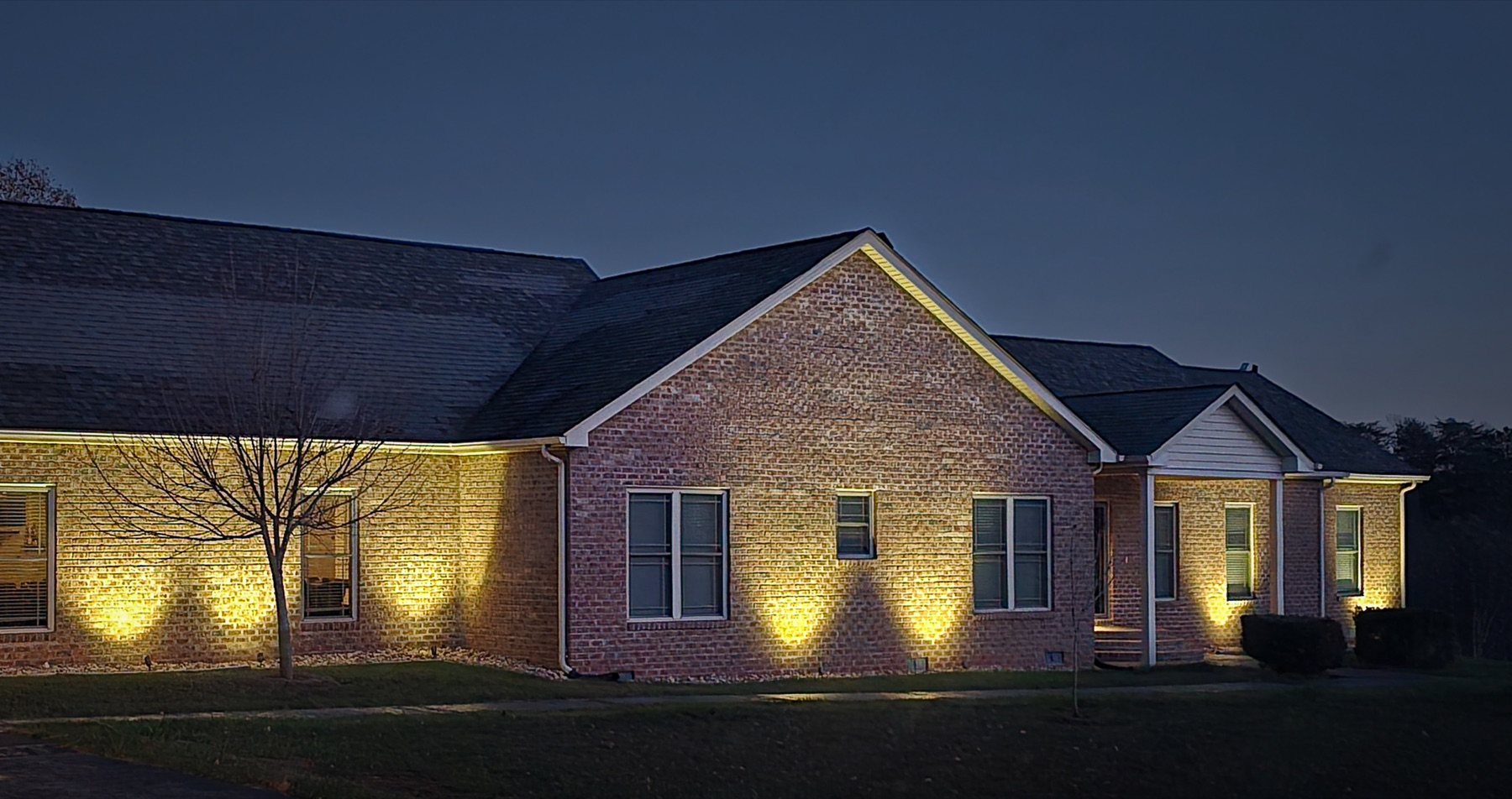 Brick home illuminated by warm exterior landscape uplights after dark