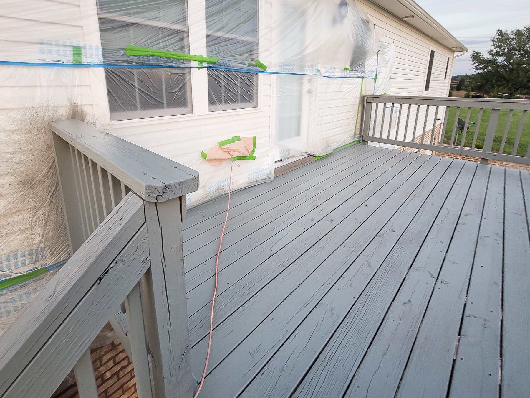 Exterior deck painting project with nearby doors and siding masked for protection