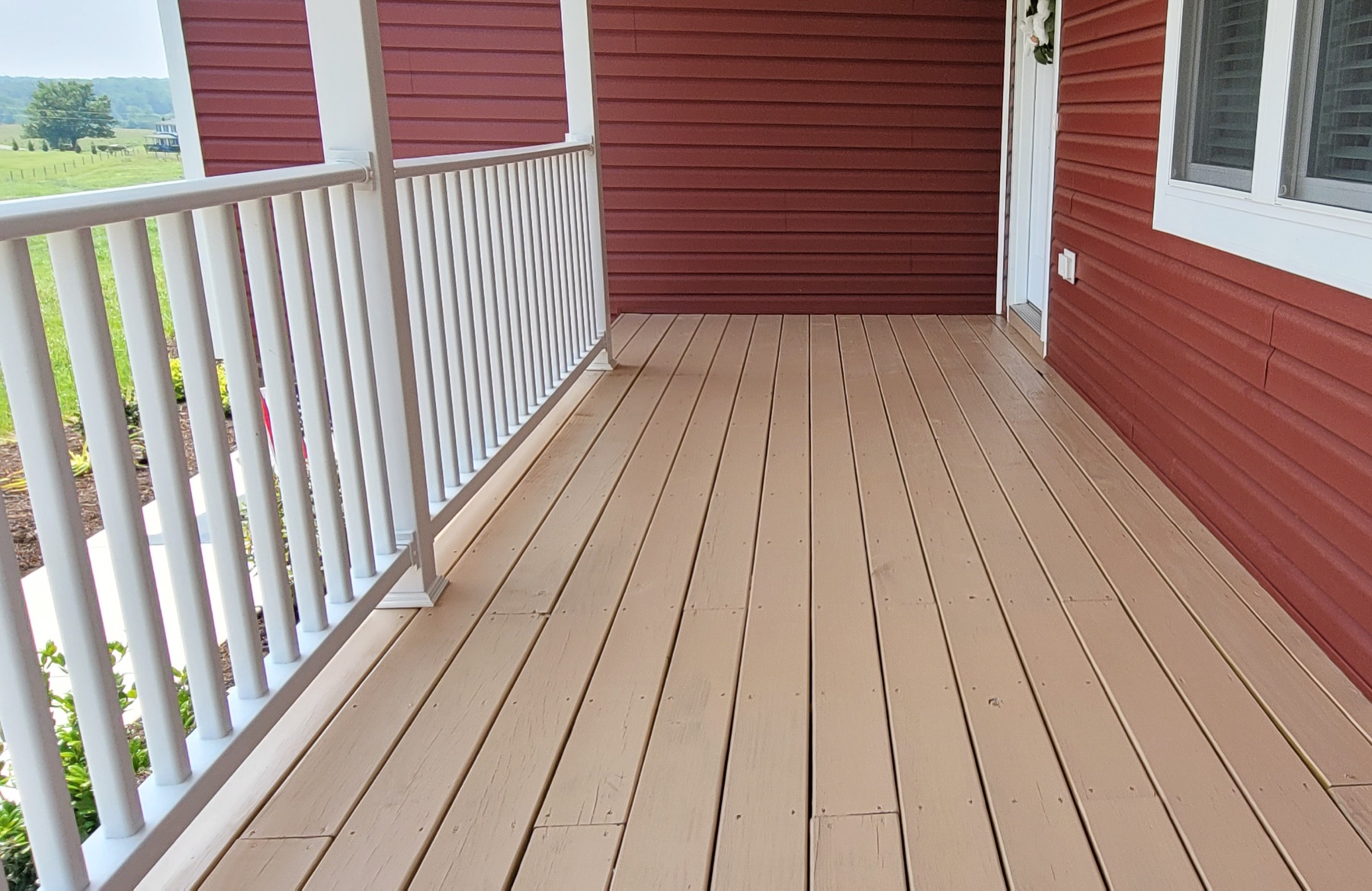 Finished painted porch beside red exterior siding and white railing